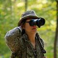 Dr. Sarah Chen, an instructor, observing wildlife through binoculars in a forest